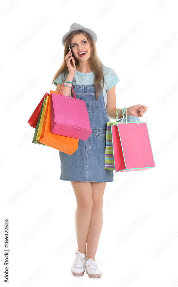 Happy young woman with shopping bags talking on phone against white background