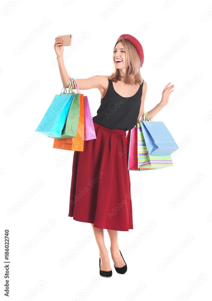 Happy young woman with shopping bags taking selfie on white background