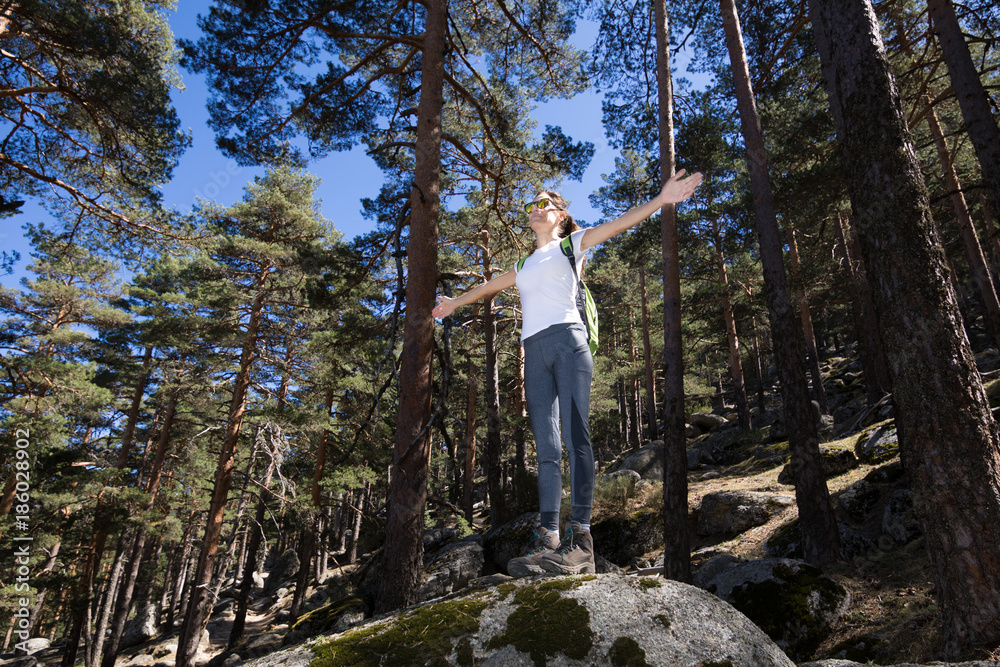 hiker sport woman standing on a great rock in the forest, open arms, in Navacerrada mountain, Guadarrama Natural Park, Madrid, Spain 
