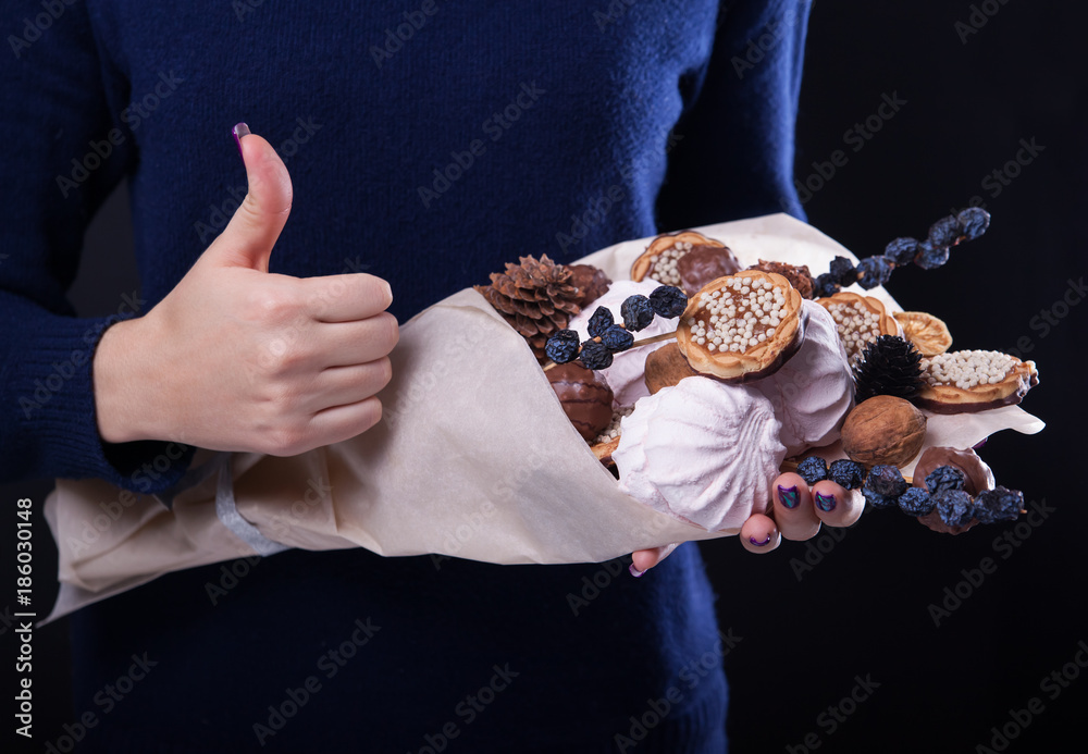 Woman holds a sweet eatable bouquet wrapped in paper on black background