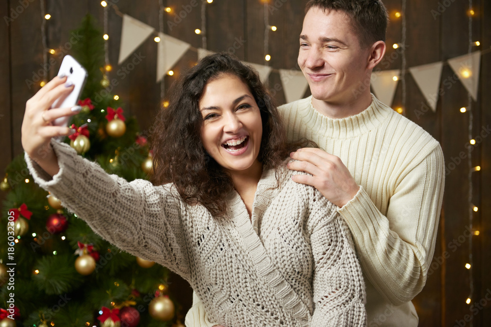 Happy couple taking selfie and having fun in christmas decoration. Dark wooden interior with lights. Romantic evening and love concept. New year holiday. Happy couple taking selfie and having fun in christmas decoration. Dark wooden interior with lights. Romantic evening and love concept. New year holiday.