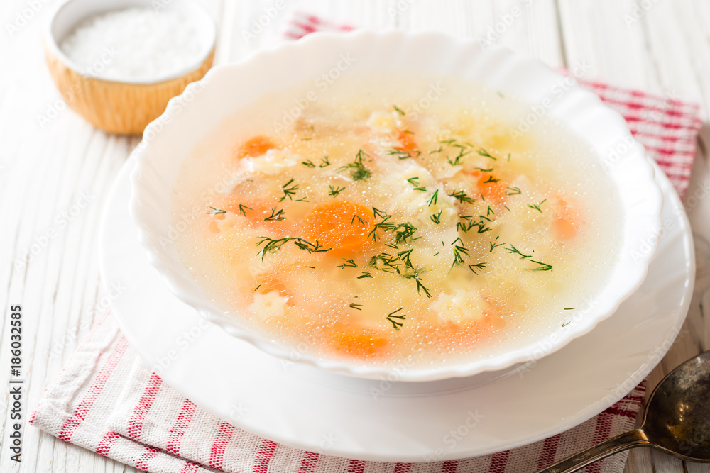 Chicken soup with stelline pasta and carrot on white wooden table.