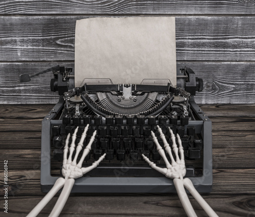 Hands of the skeleton prints on a vintage typewriter. Empty sheet of old paper for your ad design text