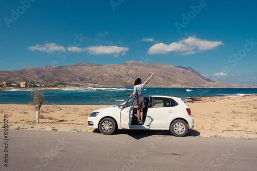 Happy young woman standing on the white car