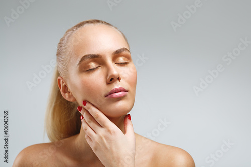 Young blond woman touching her perfect skin with her eyes closed