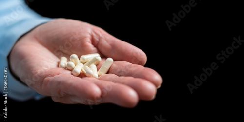 White medication capsules of glucosamine, healthy supplement pills in woman palm hand, on black background