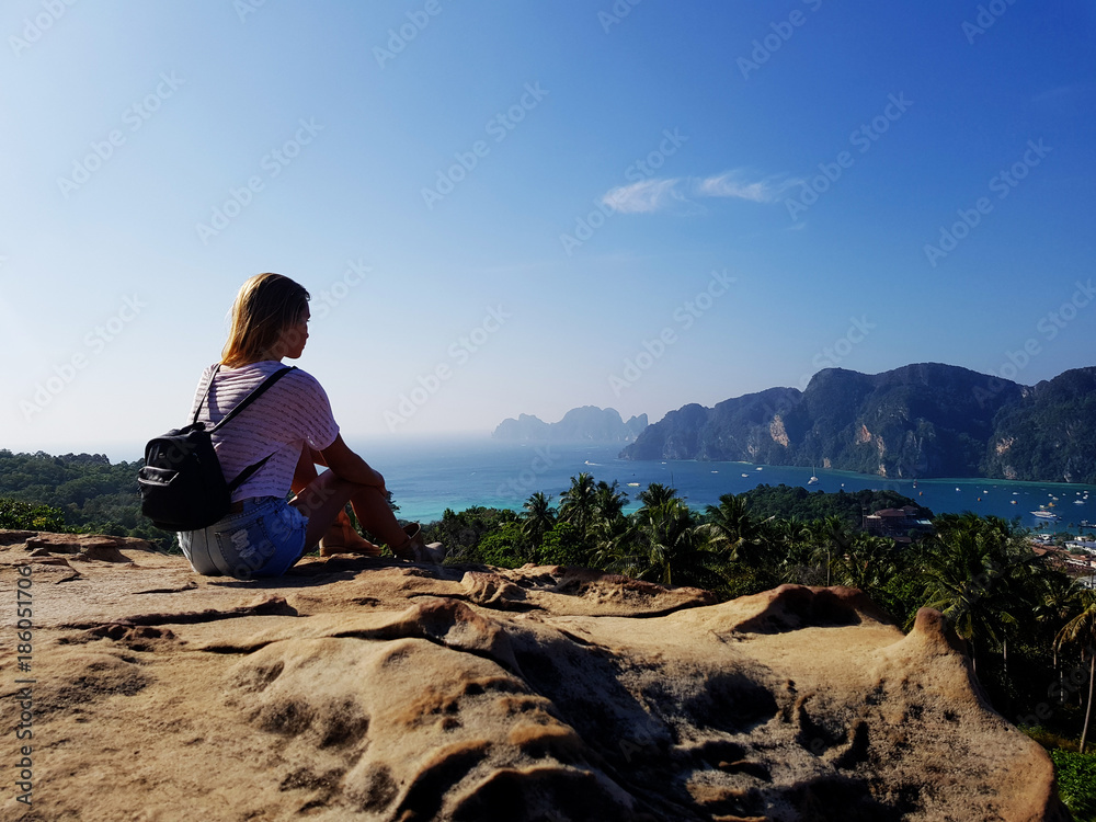 Silhouette woman sitting on the top of mountain over blue sea and sky background
