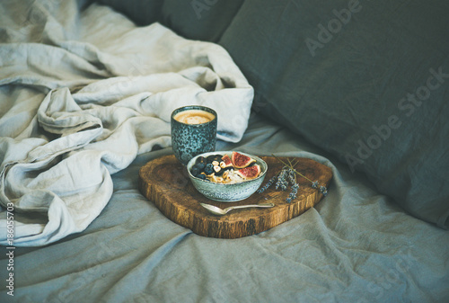 Healthy winter breakfast in bed. Rice coconut porridge with figs, berries and hazelnuts and cup of espresso over rustic wooden board background. Clean eating, alkiline diet, vegan food concept photo