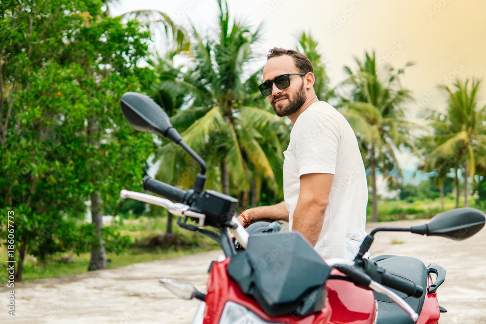 Brutal man sitting on his motorcycle on palm background