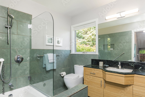 Beautiful modern bathroom with glass shower  green tiles and black marble counter top.