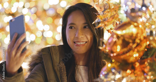 Woman taking selfie on cellphone over christmas tree decoration at night