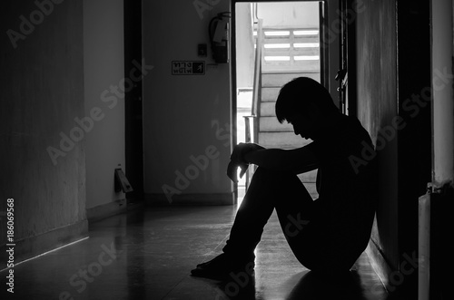 Silhouette of man sitting alone,Sad and Serious Man sitting hug his knee alone of close condo., Dramatic moment. with copy space