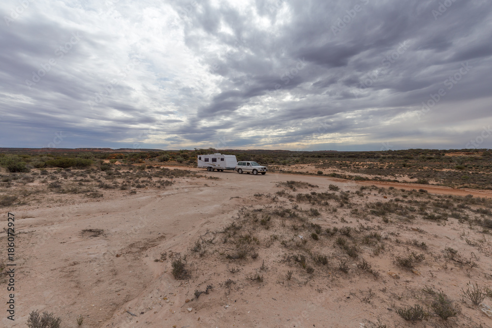 Four wheel drive vehicle  and large caravan parked on an outback road under a cloudy sky.