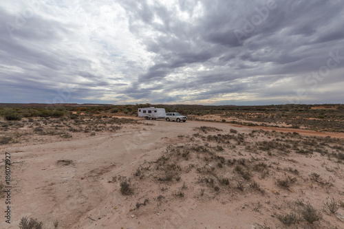 Four wheel drive vehicle  and large caravan parked on an outback road under a cloudy sky.