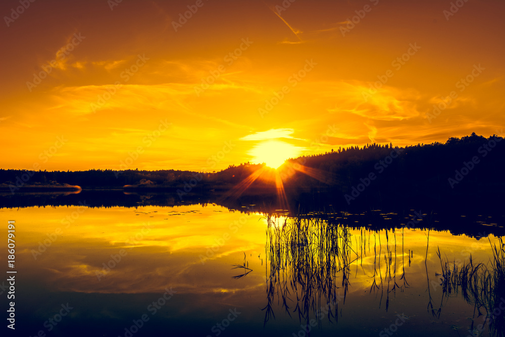 Summer landscape with sunset on the lake. Beautiful orange sundown or sunrise over forest and peaceful water with reflection of sun light, warm scenery in nature.