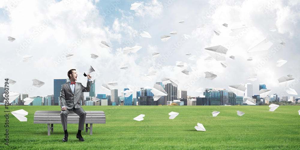 Businessman in summer park announcing something in loudspeaker and paper planes flying around