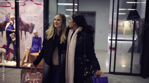 Two cute young adolescent women, heavy loaded with christmas gifts,  shopping, while walking along store windows and choosing and admiring the items. 