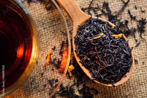 Tea leaves in a wooden spoon next to a cup of brewed tea on a background of burlap