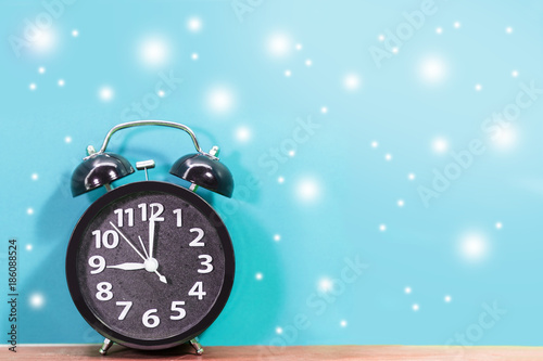 Black alarm clock with flying snow on blue background.