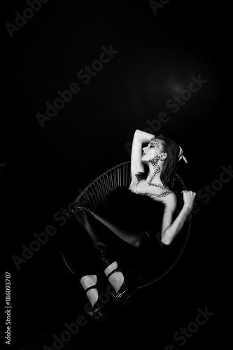 Fashion model red haired girl with originally make up like leopard predator isolated on black. Studio portrait on chair.