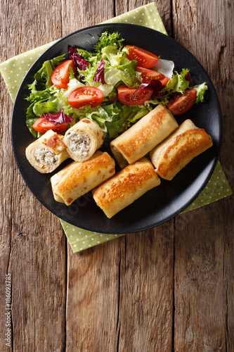 Tasty food: crepes rolls with chicken and mushrooms and vegetable salad on a plate close-up. Vertical top view