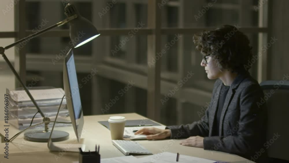 Businesswoman writing on document and drinking coffee from disposal cup in the office at night Businesswoman writing on document and drinking coffee from disposal cup in the office at night
