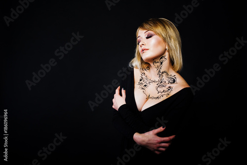 Studio portrait of blonde girl with originally make up on neck, wear on black dress at dark background.