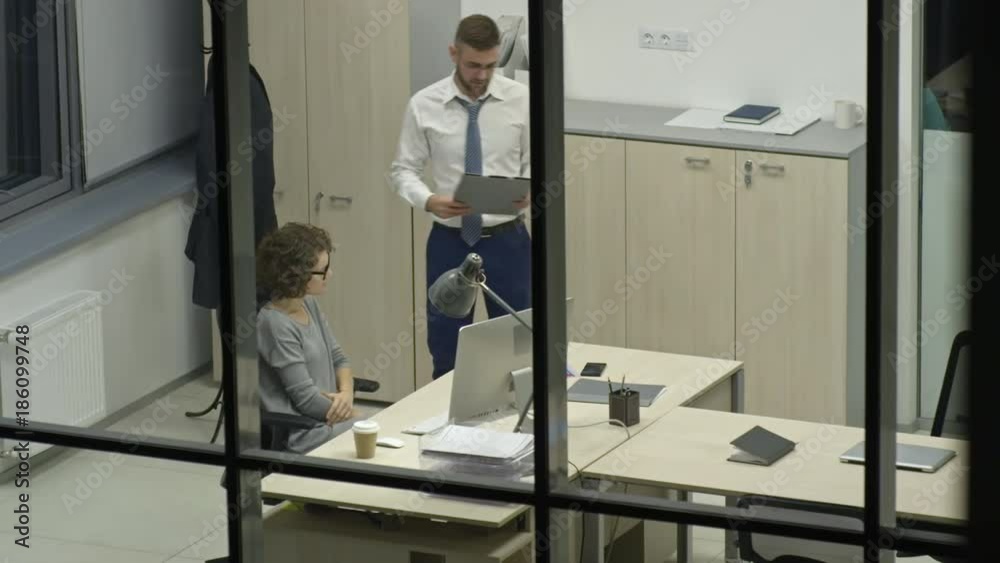 View through glass wall of man and woman discussing business project at night in the office View through glass wall of man and woman discussing business project at night in the office