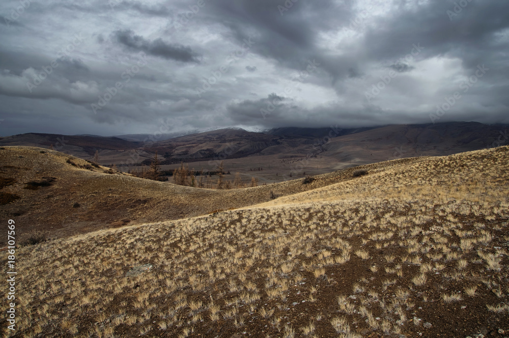 Dramatic winter dark desert steppe on a highland mountain plateau with ranges of  snow peaks on a horizon storm skyline Kurai Altai Mountains Siberia Russia