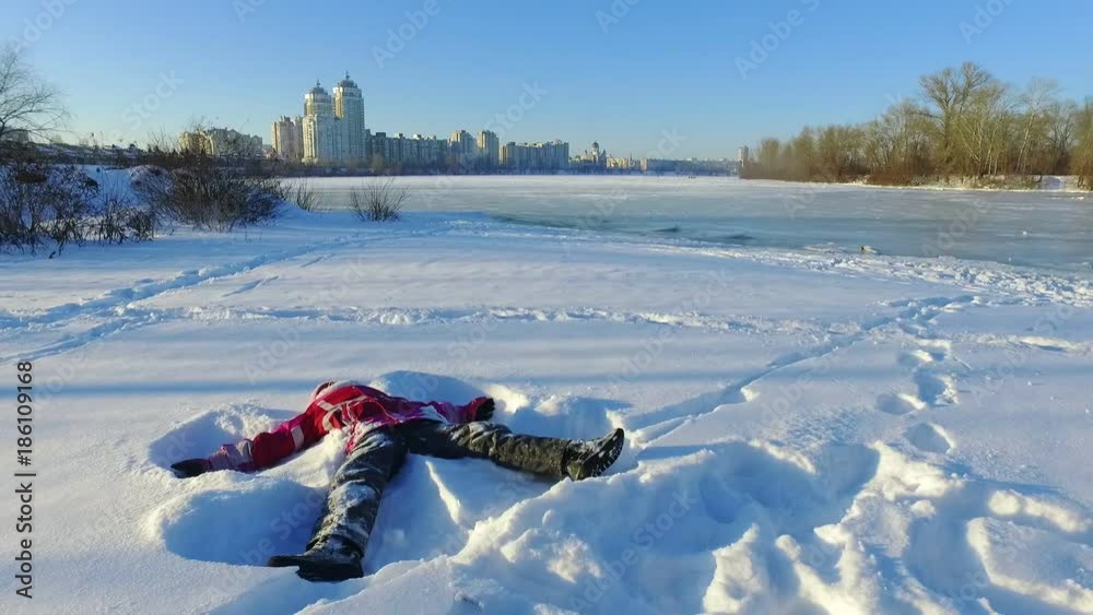 Happy little girl lying on snow in city park. Winter wonderland time. Fun snow angel in slow motion. Happy winter holiday. Snow playing