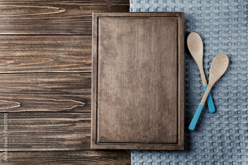 Clean kitchen towel, board and spoons on wooden table, top view