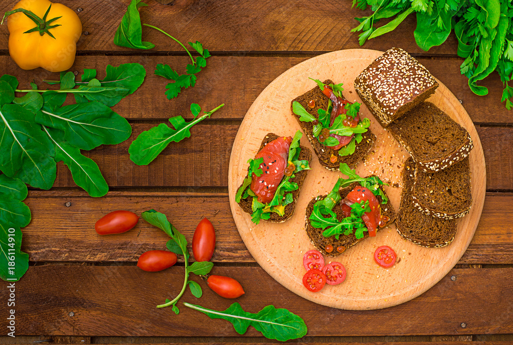 Bruschetta with salmon, red fish, red caviar, arugula and tomatoes on a board. Wooden rustic background. Selective focus. Top view Bruschetta with salmon, red fish, red caviar, arugula and tomatoes on a board. Wooden rustic background. Selective focus. Top view