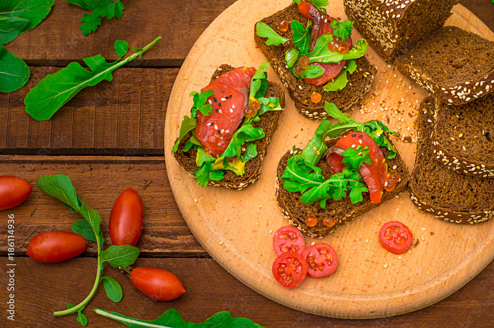 Bruschetta with salmon, red fish, red caviar, arugula and tomatoes on a board. Wooden rustic background. Selective focus. Top view Bruschetta with salmon, red fish, red caviar, arugula and tomatoes on a board. Wooden rustic background. Selective focus. Top view