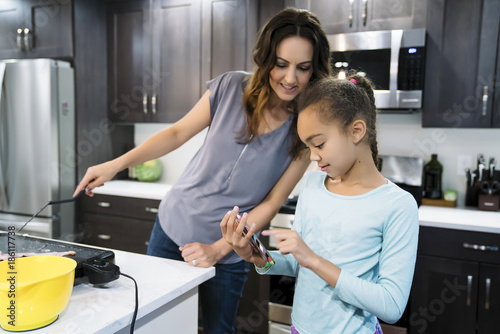 Mom looking at something on daughter's smart phone while cooking 