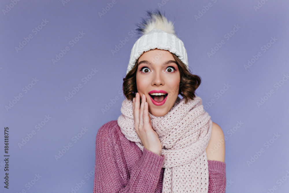 Studio portrait of charming caucasian girl in cute winter clothes. Indoor photo of winsome female model in knitted scarf fooling around on purple background. Studio portrait of charming caucasian girl in cute winter clothes. Indoor photo of winsome female model in knitted scarf fooling around on purple background.