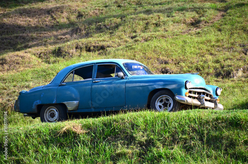 blauer Oldtimer fährt auf der Landstraße umgeben von Wiesen im Öko Dorf Las Terrazas auf Kuba 