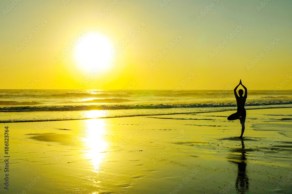 silhouette of unknown unrecognizable woman standing on beach sea water practicing yoga and meditation looking to the sun on the horizon