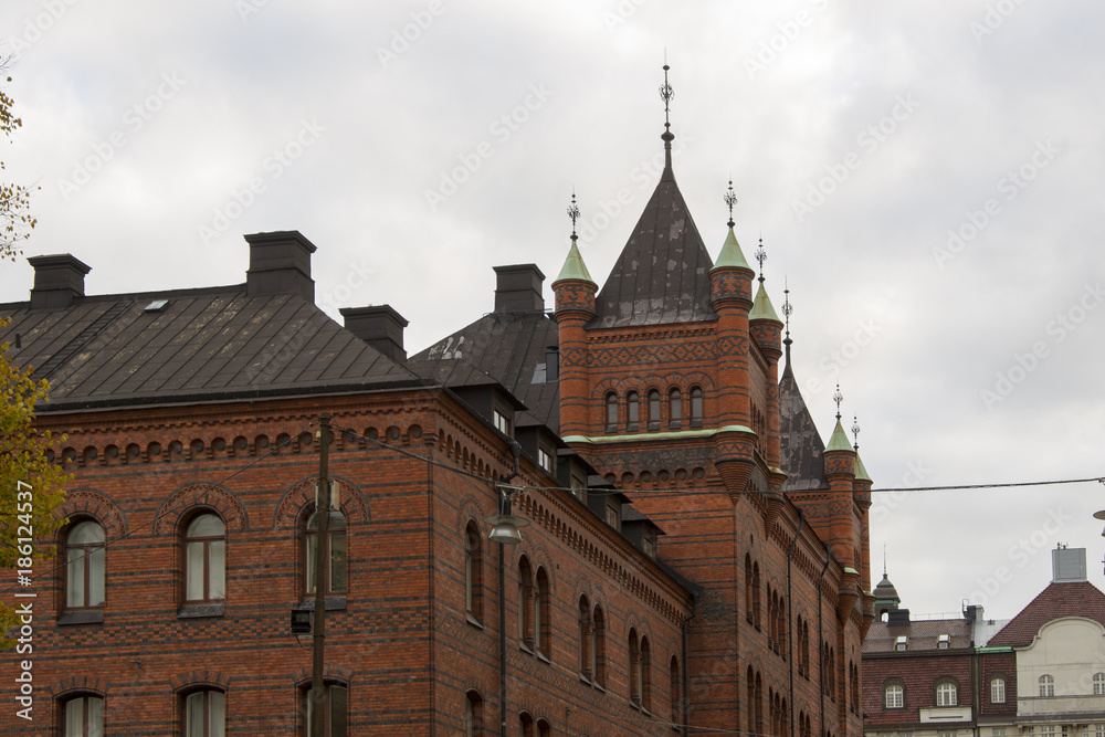 Architectural detail of facades of historic red brick houses with turrets in Stockholm, Sweden in a rooftop view against a grey cloudy sky