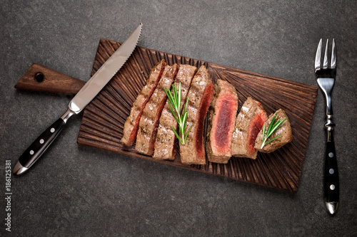 Beef steak on cutting board with rosemary and spices. Grilled meat rare steak top view