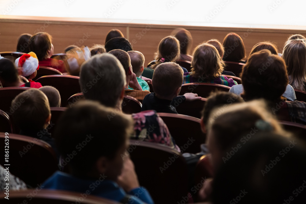 People, parents with children in the audience watching a children's show. Sold out. Shooting from the back.