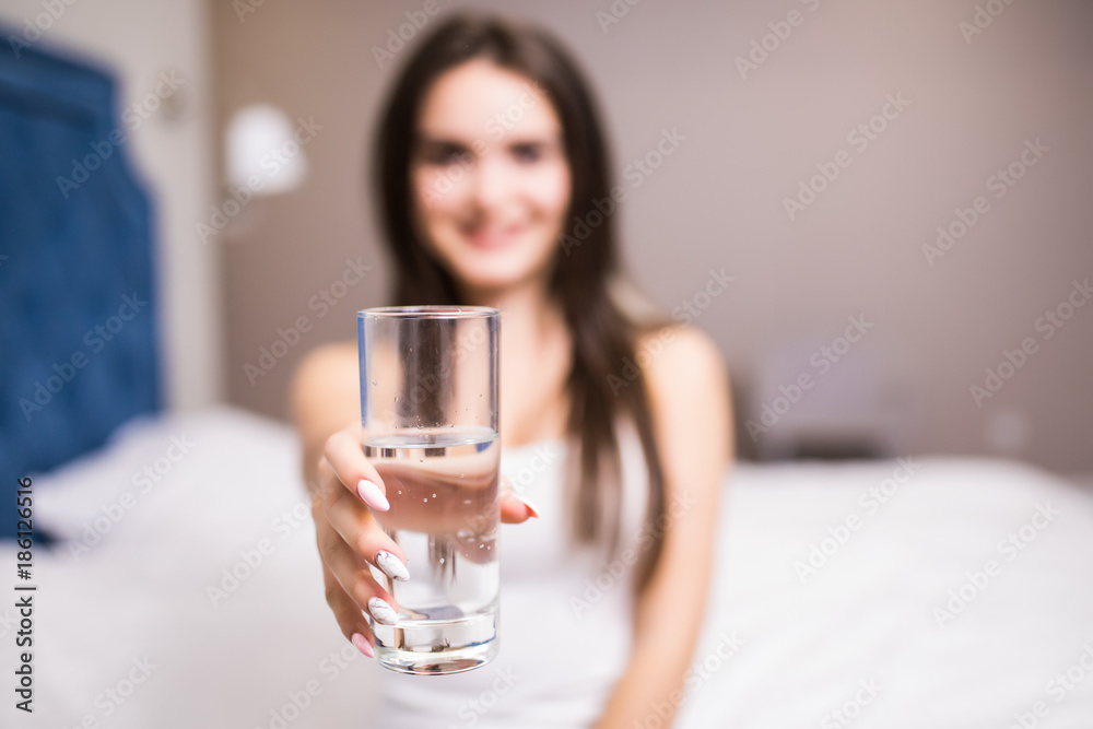 Woman hold water glass, seat in bed at home