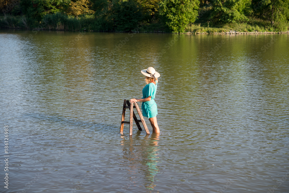 Girl standing in lake in dress and hat Girl standing in lake in dress and hat