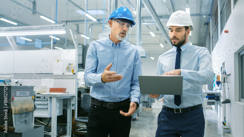 Head of the Department Holds Laptop and Discuss Product Details with Chief Engineer while They Walk Through Modern Factory.