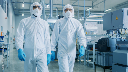 Two Engineers/ Scientists in Hazmat Sterile Suits Walking Through Technologically Advanced Factory/ Laboratory. Clean High-Tech Environment with CNC Machinery. photo