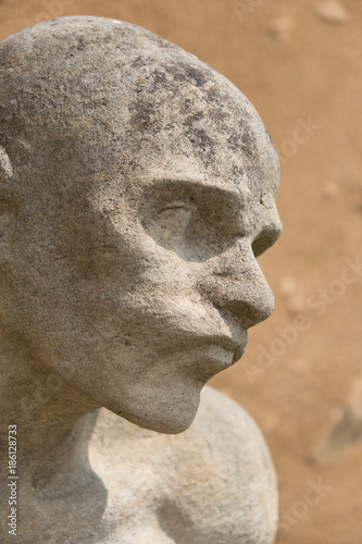 Ancient statue of a man in Cesky Krumlov, Czech Republic. Close up of statue of a man, bald, weathered and crumbling with a yellow rock textured wall in the background.