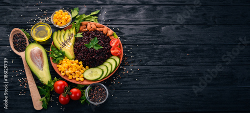 Black rice, avocado, cucumber, corn and almonds. On a wooden background. Top view. Free space for your text.