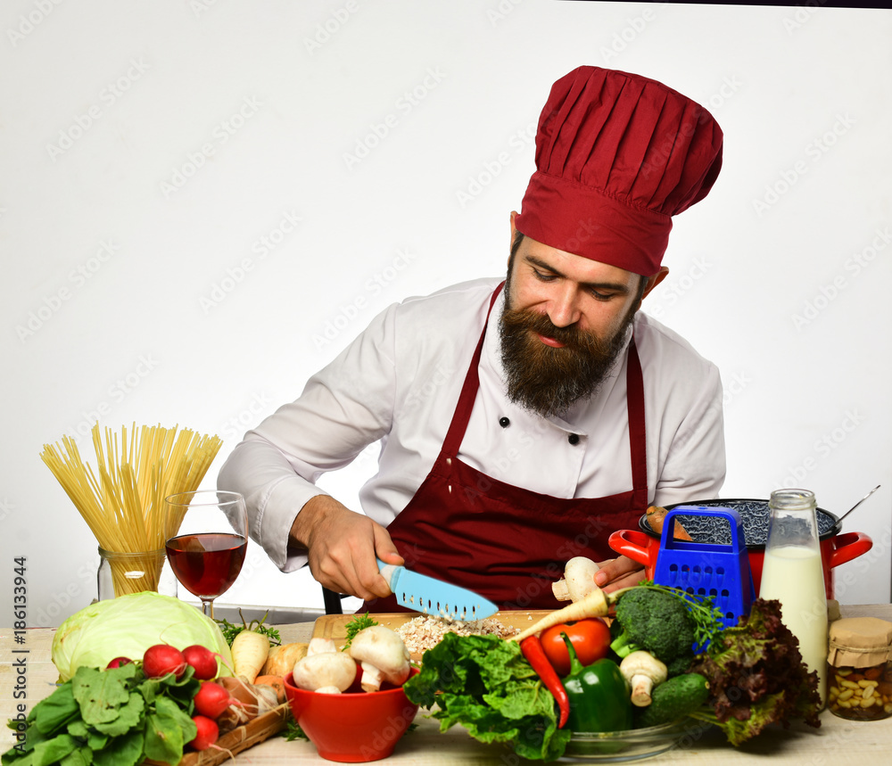 Cook with smiling face in burgundy uniform sits by table Cook with smiling face in burgundy uniform sits by table