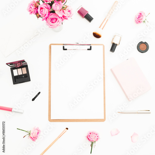 Woman workspace with pink roses bouquet, cosmetics, diary and clipboard on white background. Top view. Flat lay. Beauty or fashion blog