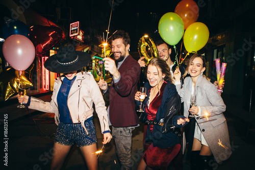 Group of happy friends going on the party, having fun at the street and drinking champagne. New year party. Birthday party 