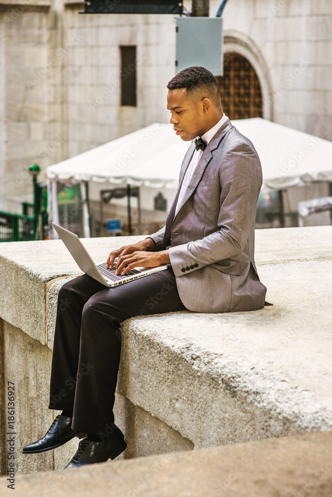 African American Businessman traveling, working in New York. Wearing gray blazer, bow tie, a college student siting on street, looking, reading, working on laptop computer. Filtered effect.. African American Businessman traveling, working in New York. Wearing gray blazer, bow tie, a college student siting on street, looking, reading, working on laptop computer. Filtered effect..